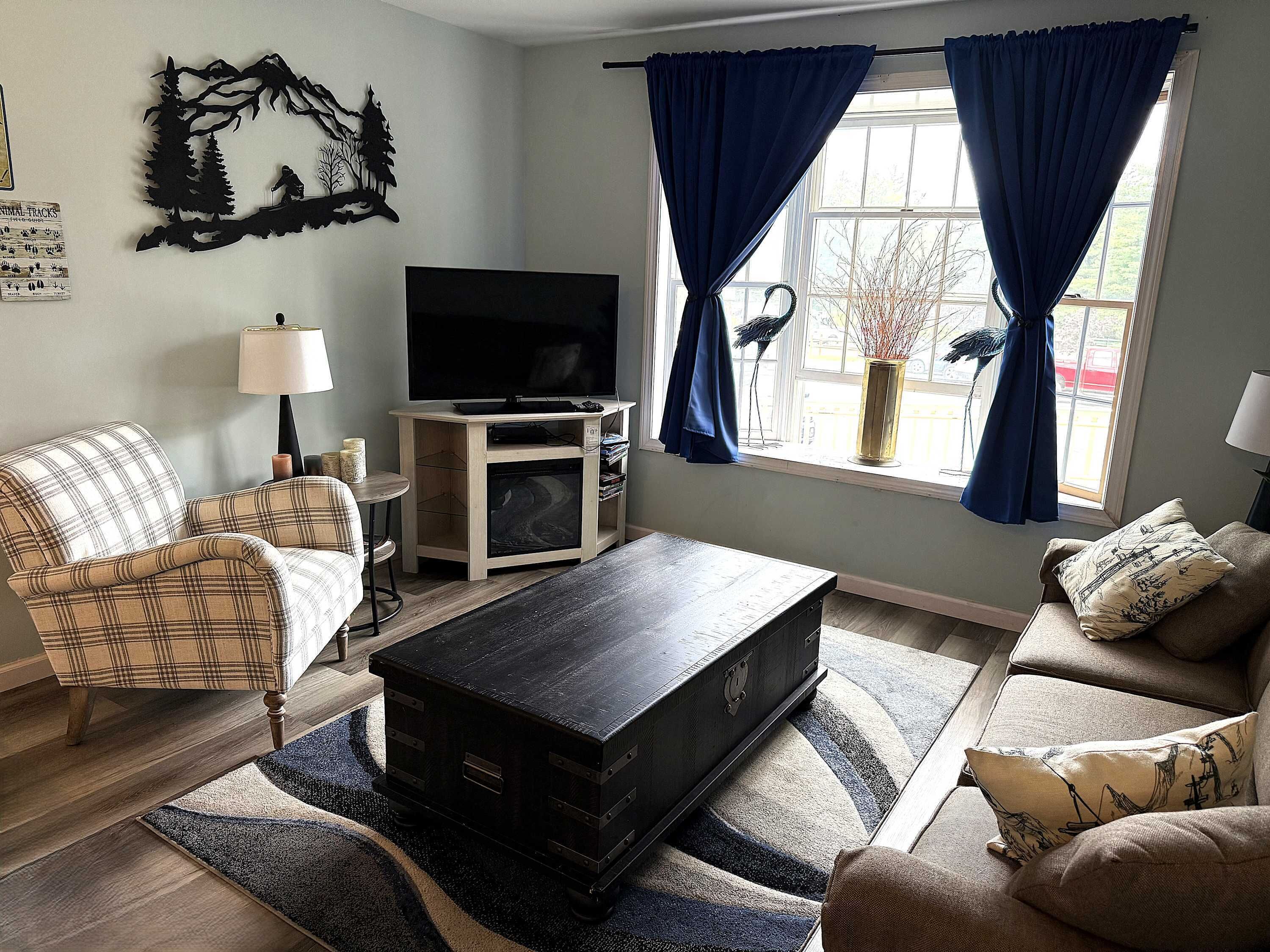 A living room with a flat-screen TV, two sofas, a coffee table, and a large window with blue curtains.