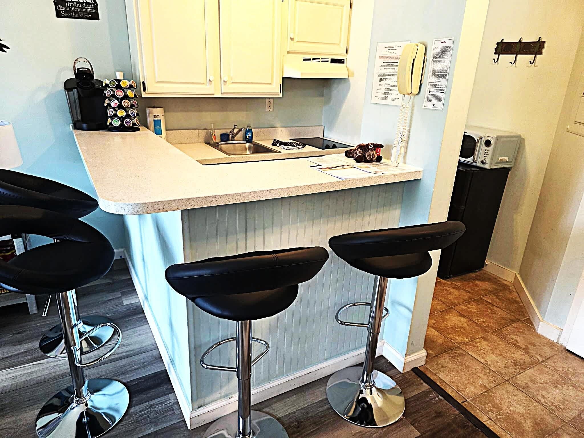 A kitchen with a bar area, including a sink, countertop, and three bar stools.