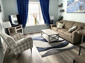 A living room with a sofa, armchair, coffee table, and a TV on a stand.