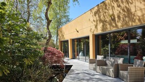 A modern outdoor patio with wicker furniture, a glass door leading to a pool, and lush greenery. - Villa indoor pool, hamman, sauna, jacuzzi, gym, billiards, baby (Plouezoc'h)