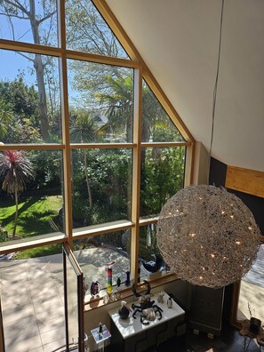 Une pièce dotée de grandes fenêtres donnant sur un jardin, d’un luminaire décoratif de forme sphérique et de diverses petites sculptures disposées sur une table.