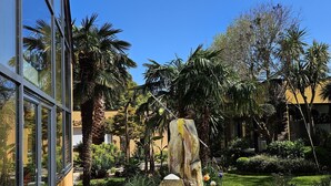 A courtyard with a large rock feature, palm trees, and a building with large windows. - Villa indoor pool, hamman, sauna, jacuzzi, gym, billiards, baby (Plouezoc'h)
