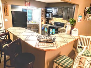 A kitchen with a central island, dark cabinets, stainless steel appliances, and a window with blinds. - White Sands Oasis:  "The Sleepy Oasis HQ, Pet Paradise, & Tealight Nights!" (Alamogordo)