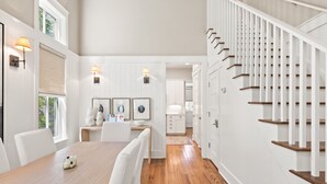 A spacious kitchen with white cabinetry, a wooden dining table, and a staircase with white railings. - Luxurious WaterColor House Minutes From Seaside and the Beach! (Santa Rosa Beach)