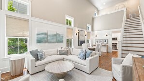 A spacious living room with a large sectional sofa, a round coffee table, and a staircase leading to an upper level. - Luxurious WaterColor House Minutes From Seaside and the Beach! (Santa Rosa Beach)