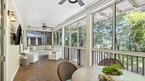 A covered porch with a wooden floor, white furniture, and large windows offering a view of trees. - Luxurious WaterColor House Minutes From Seaside and the Beach! (Santa Rosa Beach)
