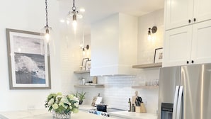 A modern kitchen with white cabinetry, a marble countertop, a stainless steel refrigerator, and pendant lighting.