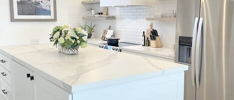 A modern kitchen with white cabinetry, a marble countertop, a stainless steel refrigerator, and pendant lighting.