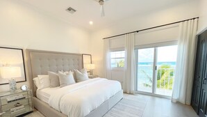 A spacious bedroom with a large bed, a nightstand with a lamp, and a view of the ocean through a sliding glass door.