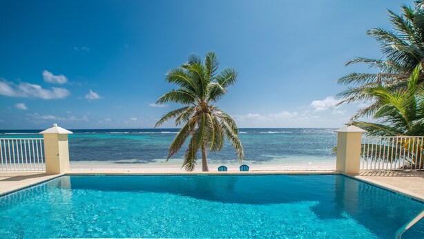 A pool with a view of the ocean, palm trees, and a '5 FT NO SWIMMING' sign.
