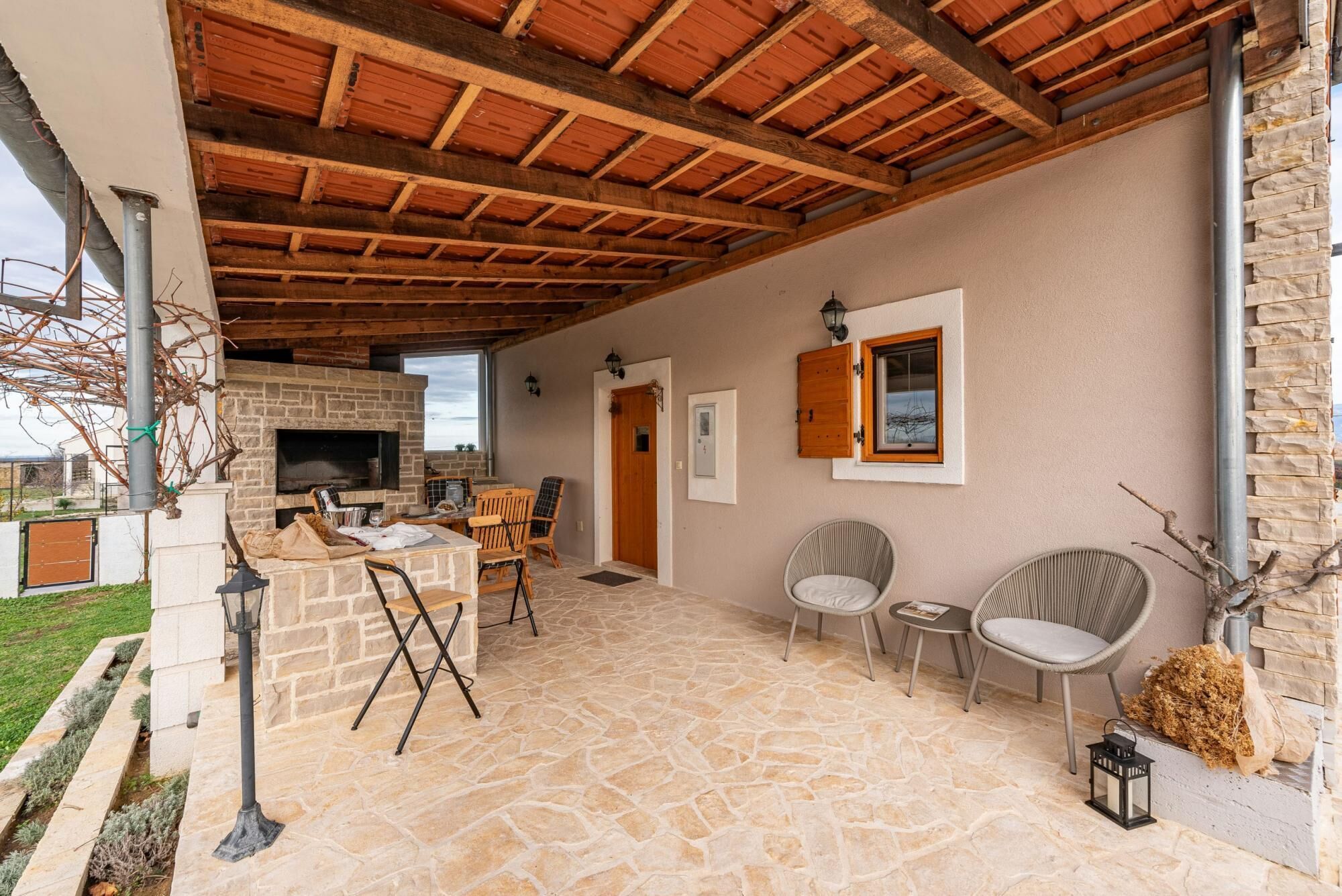 A stone-floored patio with a stone fireplace, wooden ceiling beams, and outdoor seating.