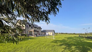 Een huis met een terras, een overdekte zithoek en een voetbalkooi in een gazon.