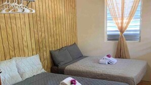 Habitación con dos camas, paneles de madera en las paredes, una ventana con cortinas y una toalla con un estampado floral en una de las camas.