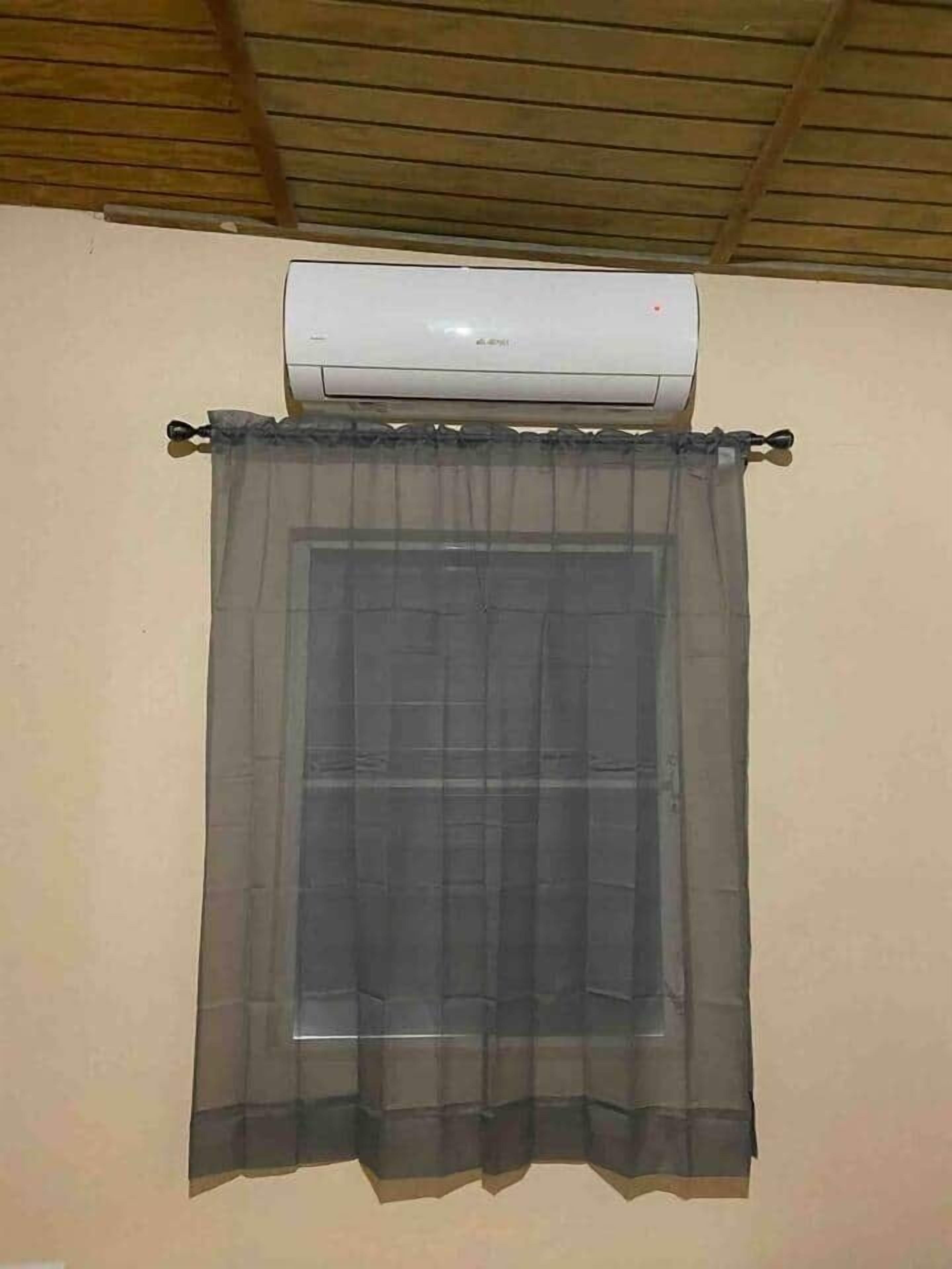 A window with a sheer curtain and an air conditioning unit above it.