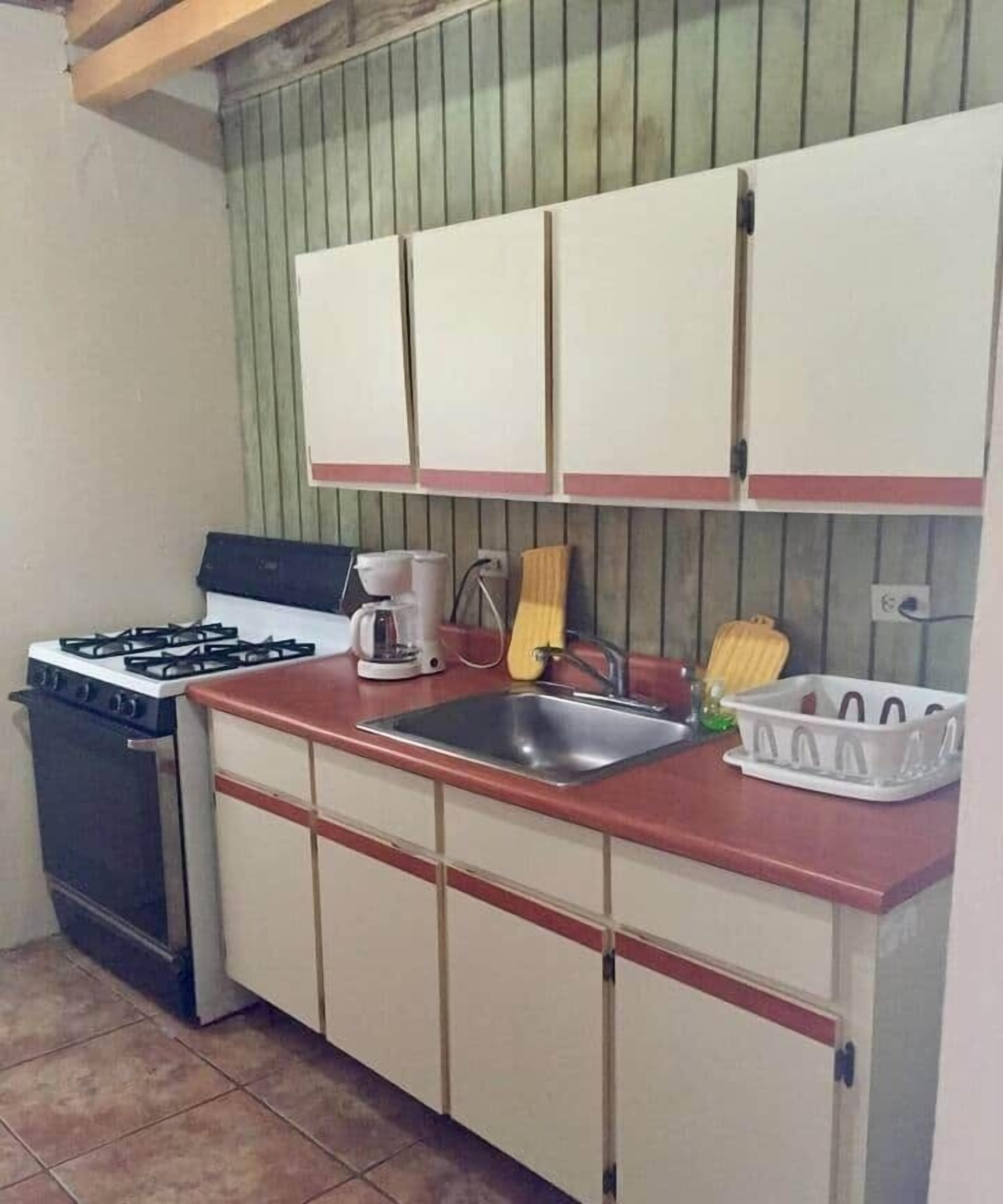 A compact kitchen with a gas stove, a sink, and cabinets.