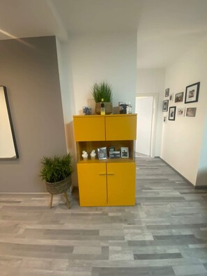 Um corredor com um armário amarelo contendo objetos decorativos e uma planta em vaso.