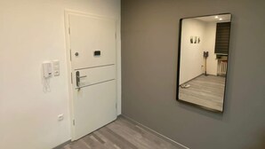Een gang met een witte deur, een spiegel aan de muur en een lichtschakelaar.