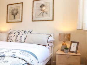 A neatly arranged bedroom with a bed, pillows, a bedside table with a lamp, and framed artwork on the wall.