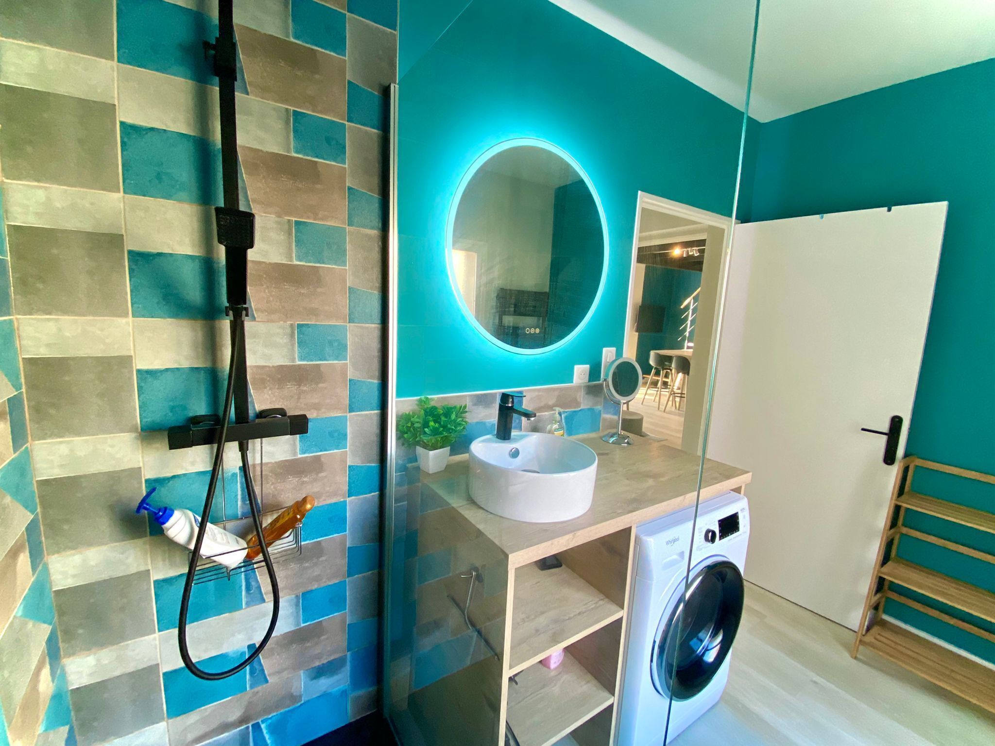 A modern bathroom with a tiled wall, a sink, a mirror, a handheld showerhead, and a washing machine.