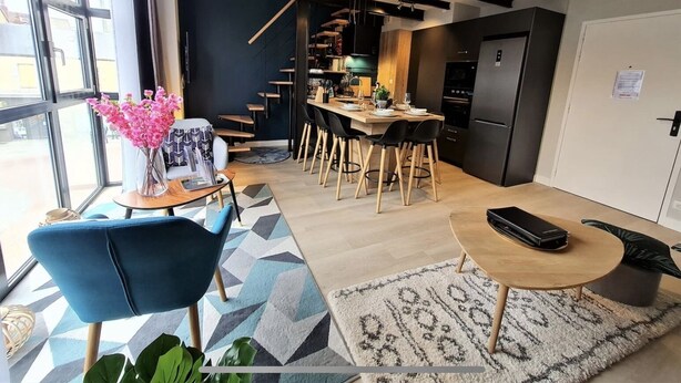 A modern kitchen with a dining area, a staircase, and a large window.