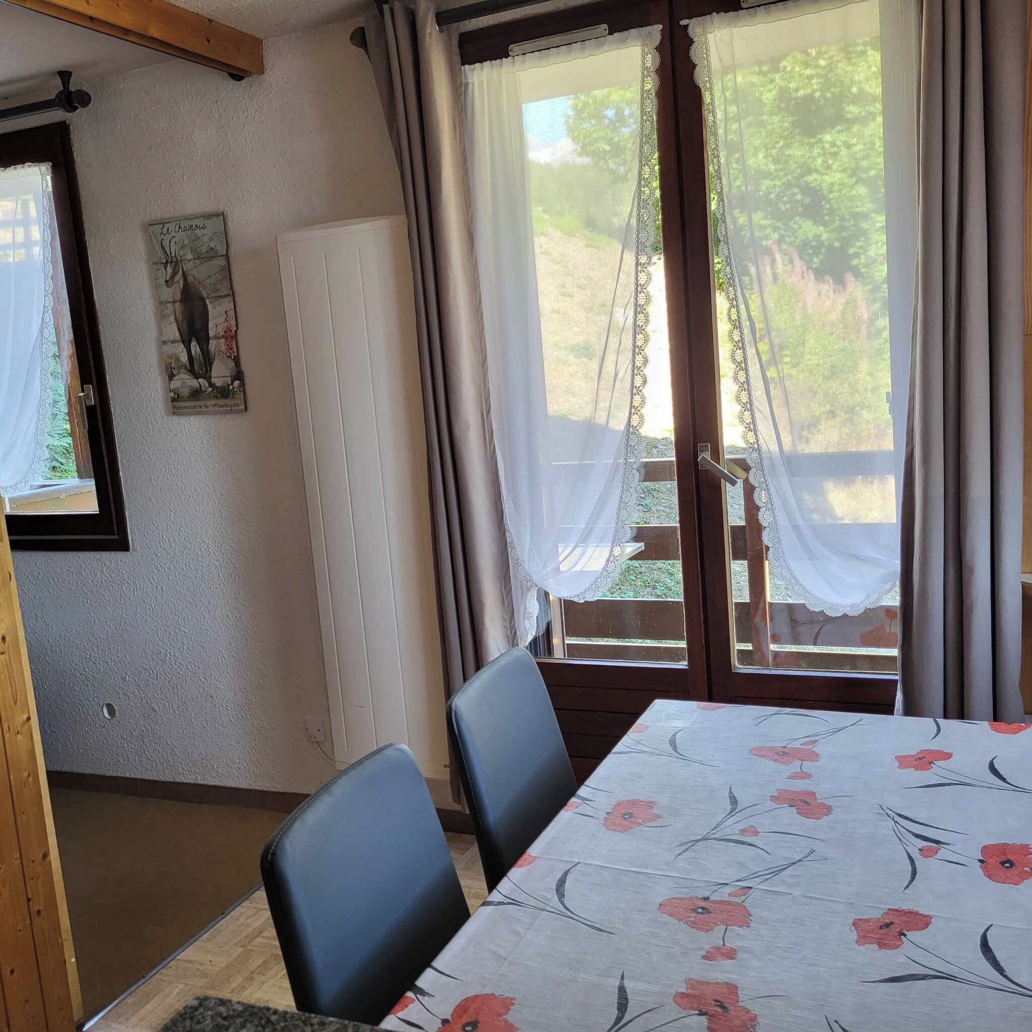 A room with a table and chairs, a radiator, a window with curtains, and a picture on the wall.