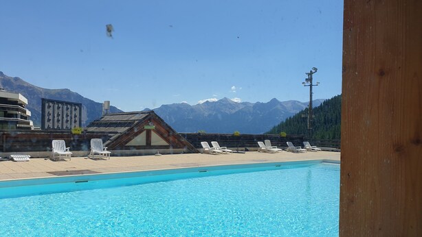 Ein Schwimmbad mit Liegestühlen, ein Holzgebäude und ein Berg im Hintergrund.