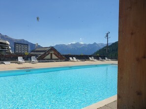 A swimming pool with lounge chairs, a wooden building, and a mountain backdrop.