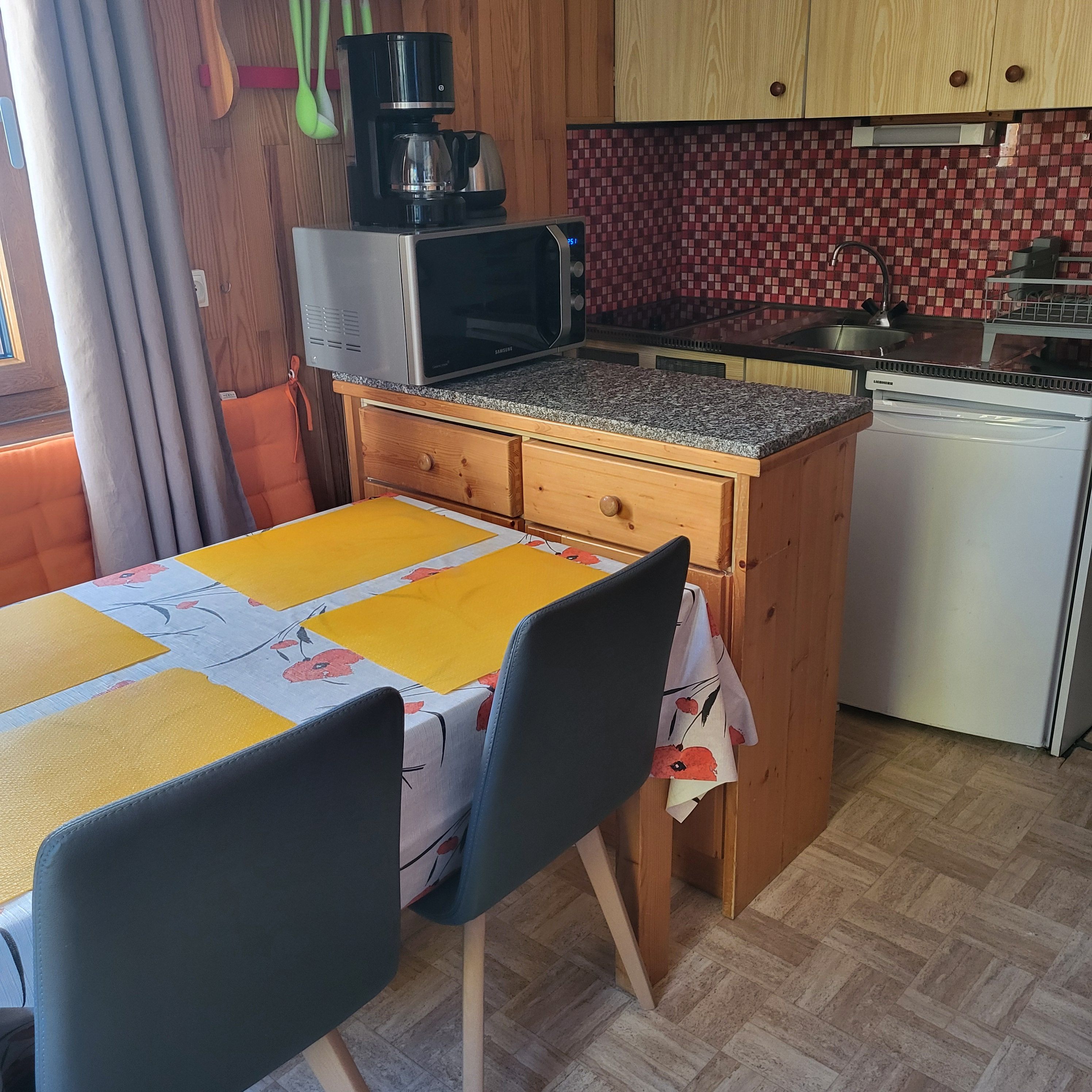 A compact kitchen with a microwave, coffee maker, and a sink. There is a table with chairs and a patterned tablecloth.