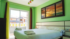 A hotel room with a bed, a nightstand, a painting, and a view of buildings through a window. - South Coast Apartment (Puertito de Güímar)