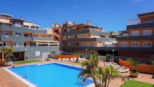 A swimming pool surrounded by a patio area with lounge chairs and palm trees. - South Coast Apartment (Puertito de Güímar)