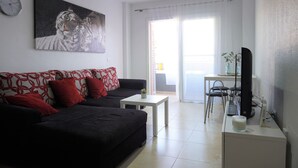 A living room with a black sofa, a white coffee table, a TV, and a painting of tigers on the wall. - South Coast Apartment (Puertito de Güímar)