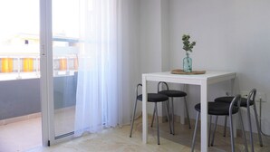 A small dining area with a white table and four chairs, a vase with a plant, and a sliding glass door to a balcony. - South Coast Apartment (Puertito de Güímar)