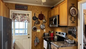 Una cocina con armarios de madera, un refrigerador de acero inoxidable, un microondas, una estufa y diversos utensilios de cocina.