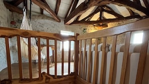 A wooden loft bedroom with a bed, a hammock, and a view of the outside.