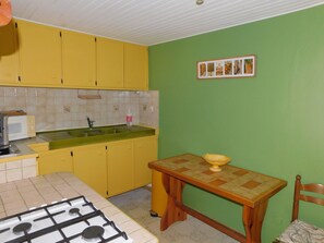 A kitchen with yellow cabinets, a green wall, a tiled backsplash, a sink, a stove, and a wooden table with a chair. - Small Provencal house independent from the Mas (Saint-Alexandre)