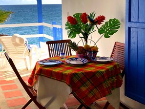 A table set for two with a colorful tablecloth, a fruit basket, and a vase with flowers. - Immaculate 1-bed Apartment on Ocean View (Philipsburg)