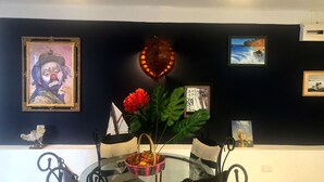 Un comedor con una mesa de vidrio, sillas y un florero con flores. En la pared hay obras de arte enmarcadas.