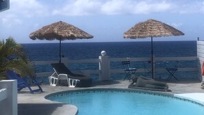 Un área de piscina con dos sombrillas de paja, sillas de descanso y vista al océano.