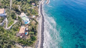 An aerial view of a coastal property with a rocky shoreline, a swimming pool, and a small building with a tiled roof. - Villa Ad Maiora in Massa Lubrense (Massa Lubrense)