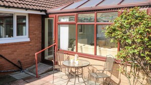 Un invernadero con techo de cristal, fachada de ladrillo y zona de patio con mobiliario exterior.