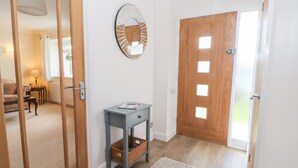 Un pasillo con puerta de madera, un espejo, una mesita con una cesta y un tapete blanco.