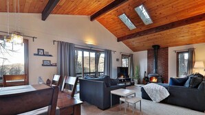 A cozy living room with a fireplace, wooden ceiling beams, and a dining area with a table and chairs. - Ski house 8 min from the mountain (Killington)