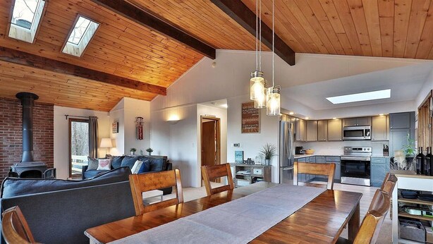 A cozy living room with a fireplace, wooden ceiling beams, and a dining area with a long table and chairs. - Ski house 8 min from the mountain (Killington)