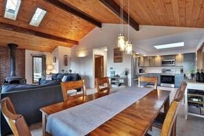 A cozy living room with a fireplace, wooden ceiling beams, and a dining area with a long table and chairs. - Ski house 8 min from the mountain (Killington)