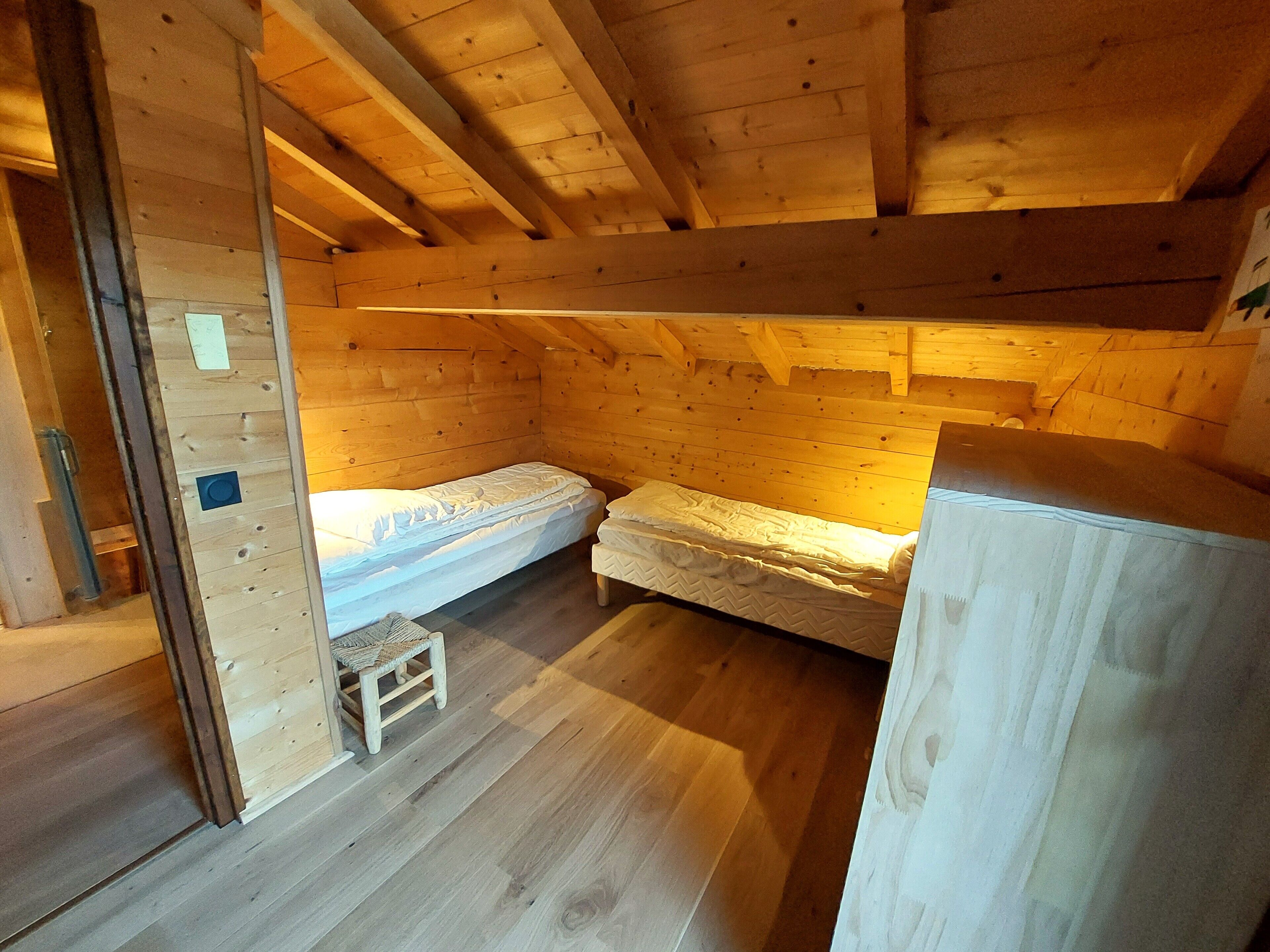 Une petite pièce en bois, aménagée comme une cabane, avec deux lits simples, un plancher en bois et un plafond en pente.