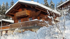 Un chalet en bois doté d’un balcon, entouré d’arbres couverts de neige.