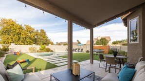 Uma área de varanda coberta com piscina, mobiliário de jardim e vista para o quintal.