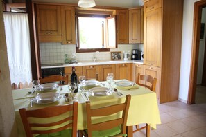Una cocina bien iluminada con armarios de madera, una mesa de comedor preparada para cuatro comensales y un ventanal sobre el fregadero.