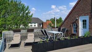 Terraço no telhado com espreguiçadeiras, mesa e vasos de plantas.