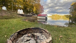 A lakeside cabin with a fire pit in the foreground, surrounded by autumn foliage and a calm lake. - Cozy Lakefront Getaway in South Frontenac, Rustic & Elegant, Highspeed Internet (Battersea)